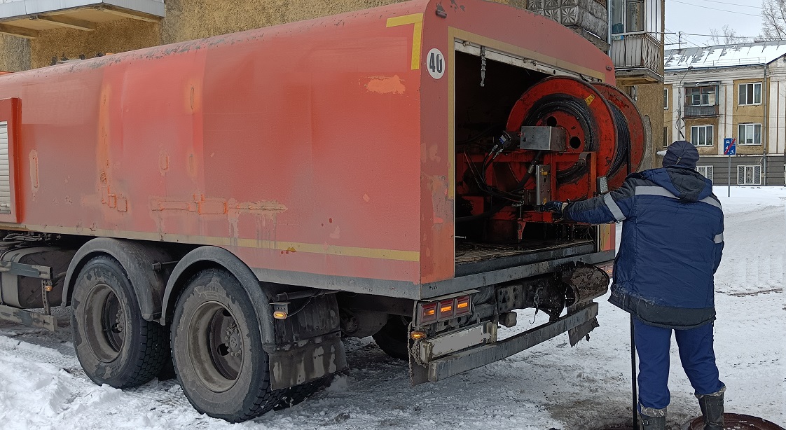 Каналопромывочная машина и работник прочищают засор в канализационной системе в Холм-Жирковском